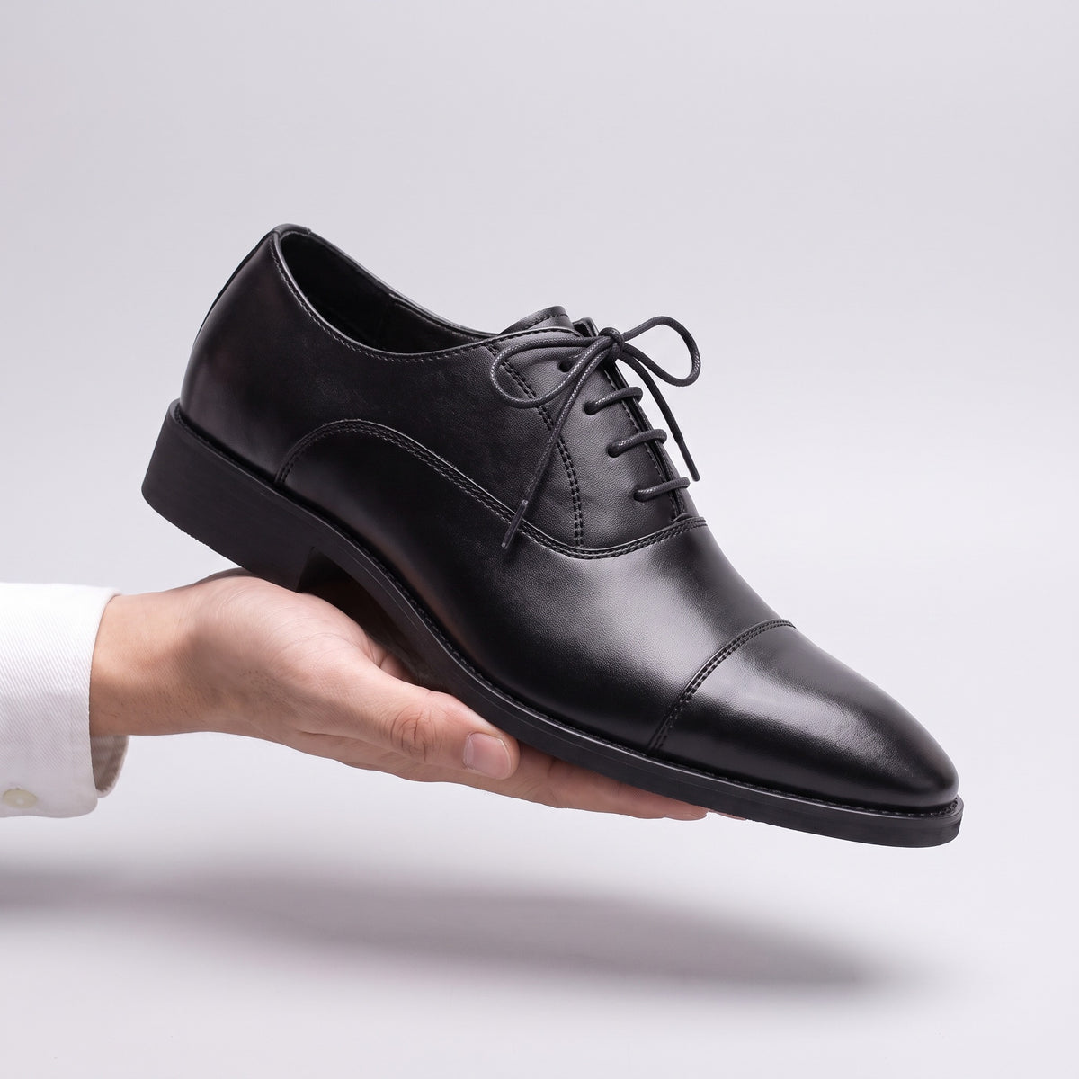 The Regent Oxford dress shoe in black, held in one hand