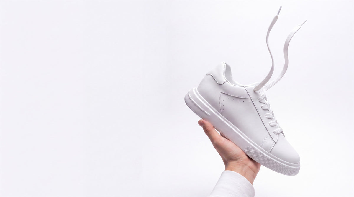 The Apex white leather sneaker held up in an open hand against a pale grey background
