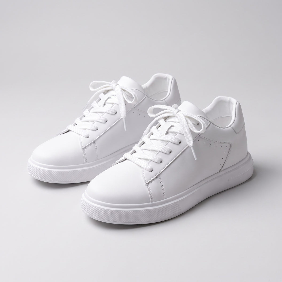 A pair of Apex white leather sneakers on a soft grey studio background