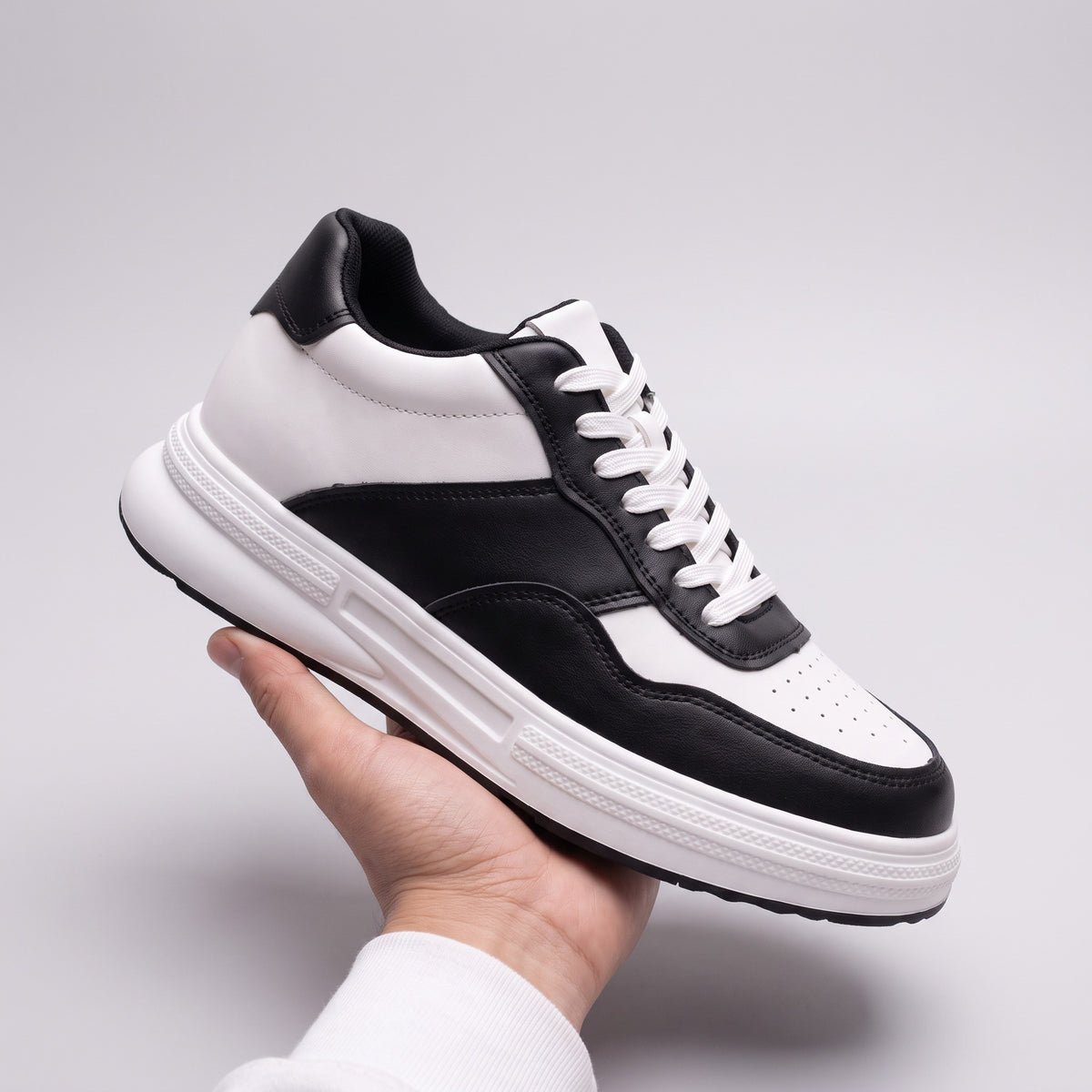 The Crest black and white leather sneaker, held in an open hand on a pale grey background